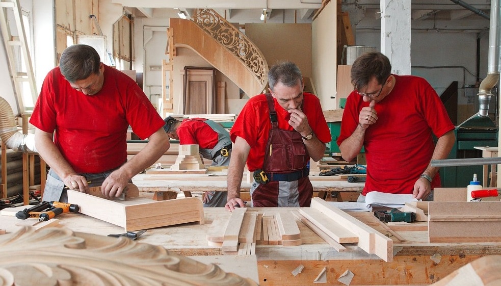 Skilled craftsmen working on custom wood furniture in the Hercigne workshop
